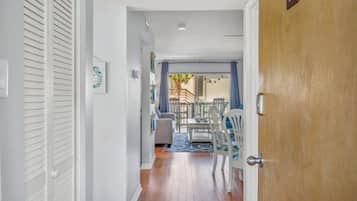 Un pasillo que lleva a un comedor con una mesa y sillas, una puerta de madera con un número, y vistas al exterior.