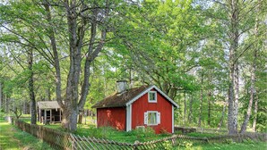 Una cabaña de madera roja rodeada por un cerco de madera y árboles.