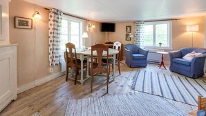 Una sala de estar acogedora con comedor, que cuenta con televisor, asientos cómodos y ventanas amplias.