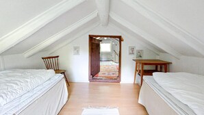 Un dormitorio pequeño tipo buhardilla con dos camas individuales, una silla de madera y una mesita.