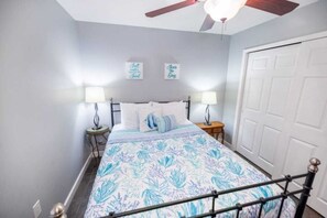 A bedroom with a bed, two bedside lamps, a ceiling fan, and a door.