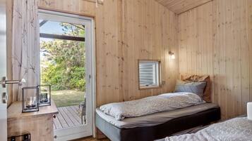 Une pièce de style cabane en bois, avec un lit, une petite fenêtre et une porte donnant sur une terrasse extérieure.