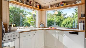 Une cuisine moderne avec des meubles blancs, une cuisinière et un lave-vaisselle. Deux fenêtres offrent une vue sur la verdure environnante.