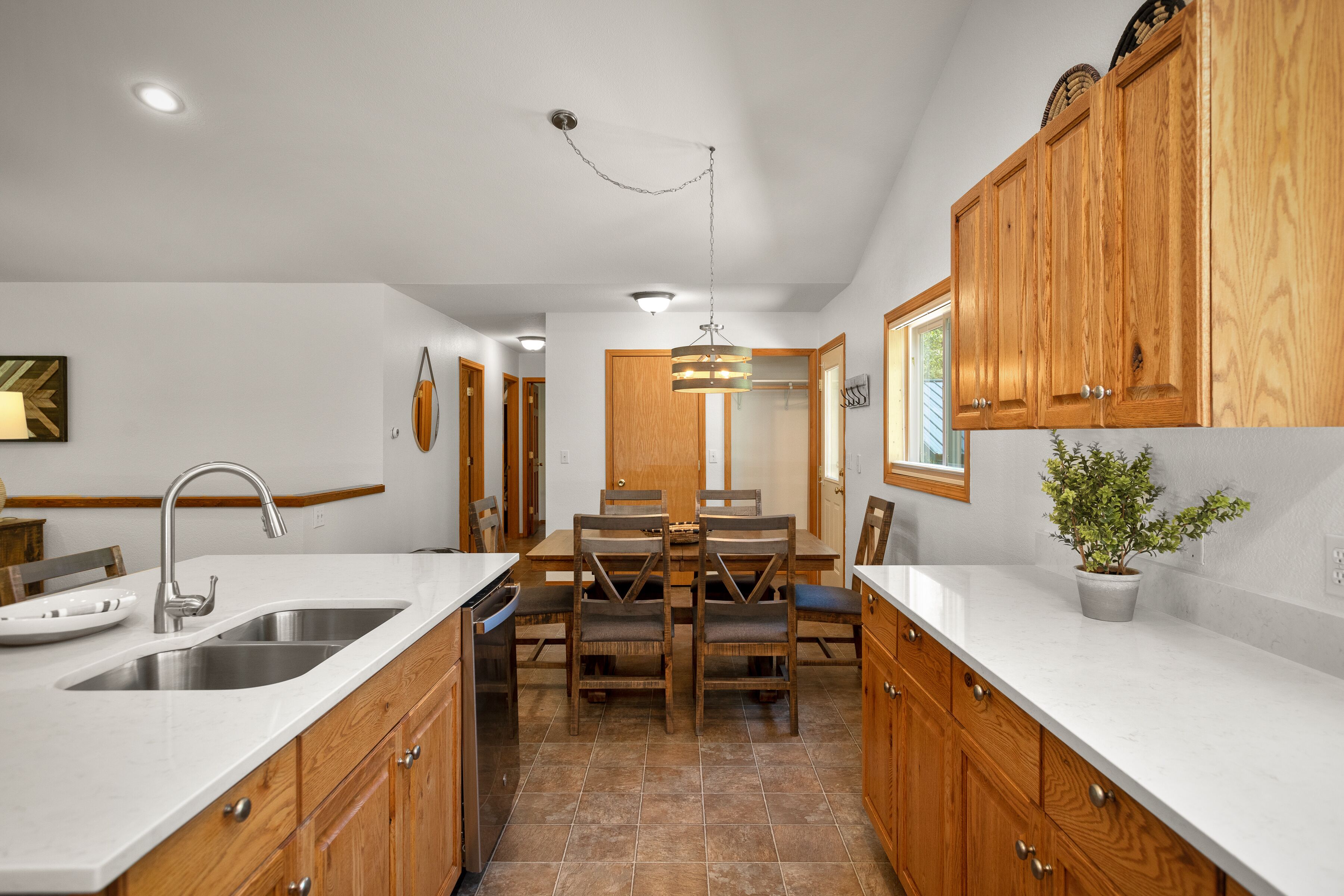 A kitchen with wooden cabinets, a white countertop, a sink, and a dining area with chairs and a table.