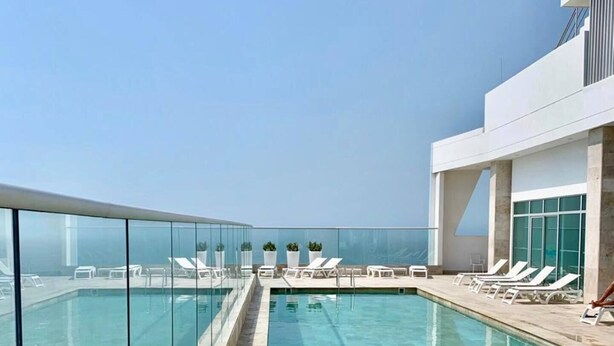 Una piscina infinitum al terrat amb aigua blau clar, envoltada de gandules blanques i una barana de vidre.
