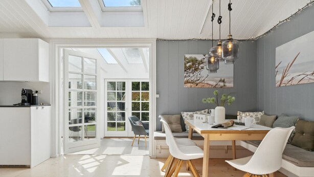 Una cocina moderna con armarios blancos, una cafetera y un comedor con mesa de madera y sillas blancas.