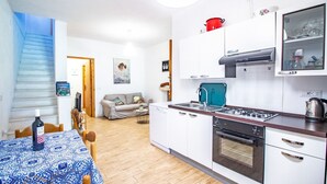 Een kleine keuken met witte kastjes, een gasfornuis en een vaatwasser. Er is een zithoek met een tafel en stoelen, en een trap naar een andere kamer.
