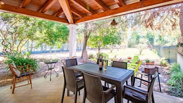 Een terras buiten met houten overkapping, een tafel met stoelen en potplanten.