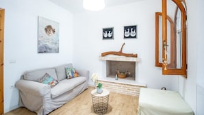 Een gezellige woonkamer met een bank, een klein rond tafeltje met een vaas, een open haard en decoratieve wandkunst.