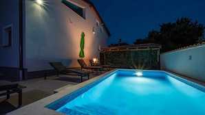 A swimming pool with a tiled edge, surrounded by lounge chairs and a table. - Beach front home in Peroj (Peroj)