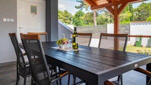 A dining area with a wooden table and chairs, a bottle of wine, and a bowl of fruit. - Beach front home in Peroj (Peroj)