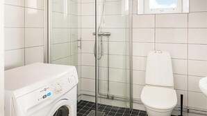 Kompakti kylpyhuone, jossa on lasiseinällä varustettu suihku, valkoinen wc-istuin ja etukuormauspesukone.