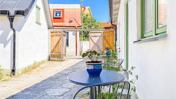 A narrow alleyway with a round metal table and chairs, a potted plant, and a wooden gate.