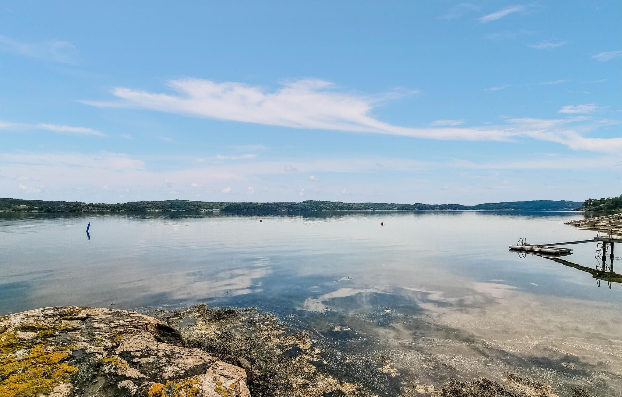 Un lago tranquillo con acque limpide, circondato da aspri pendii rocciosi e colline lontane.