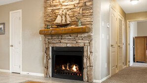 A stone fireplace with a ship model above it, a wooden mantel, and a fire burning inside. - Combined Condo & Suite with Lock-off Access at StoneBridge (Reeds Spring)