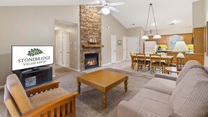 A living room with a fireplace, a television, and a dining area with chairs and a table. - Golf Condo with Fireplace & Jetted Tub at StoneBridge Village (Reeds Spring)