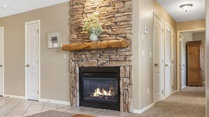 A living room with a stone fireplace, a wooden bench, and a hallway leading to another room. - Perfect for a Couple! Condo at StoneBridge Village Resort (Reeds Spring)
