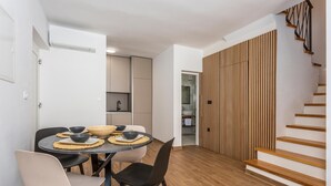 Une cuisine moderne avec des meubles blancs, un escalier en bois et un coin repas comprenant une table ronde et des chaises.