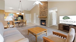 A spacious living room with a fireplace, a dining area, and a kitchen in the background.