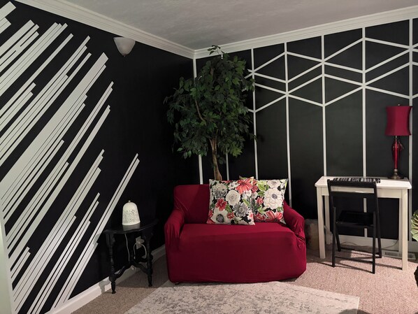 Una habitación con sofá rojo, lámpara blanca, pared con diseño blanco y negro y un motivo geométrico en la pared.