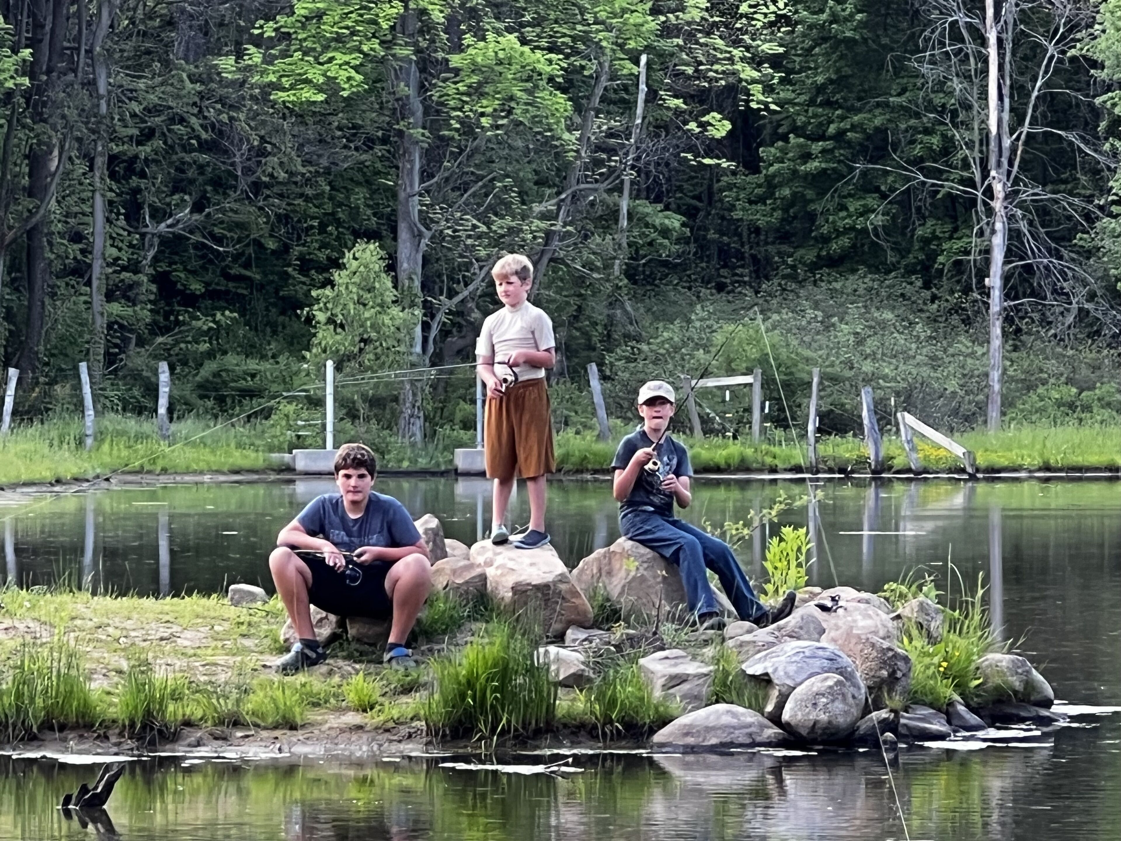 Three individuals by a calm pond with rocks and greenery.