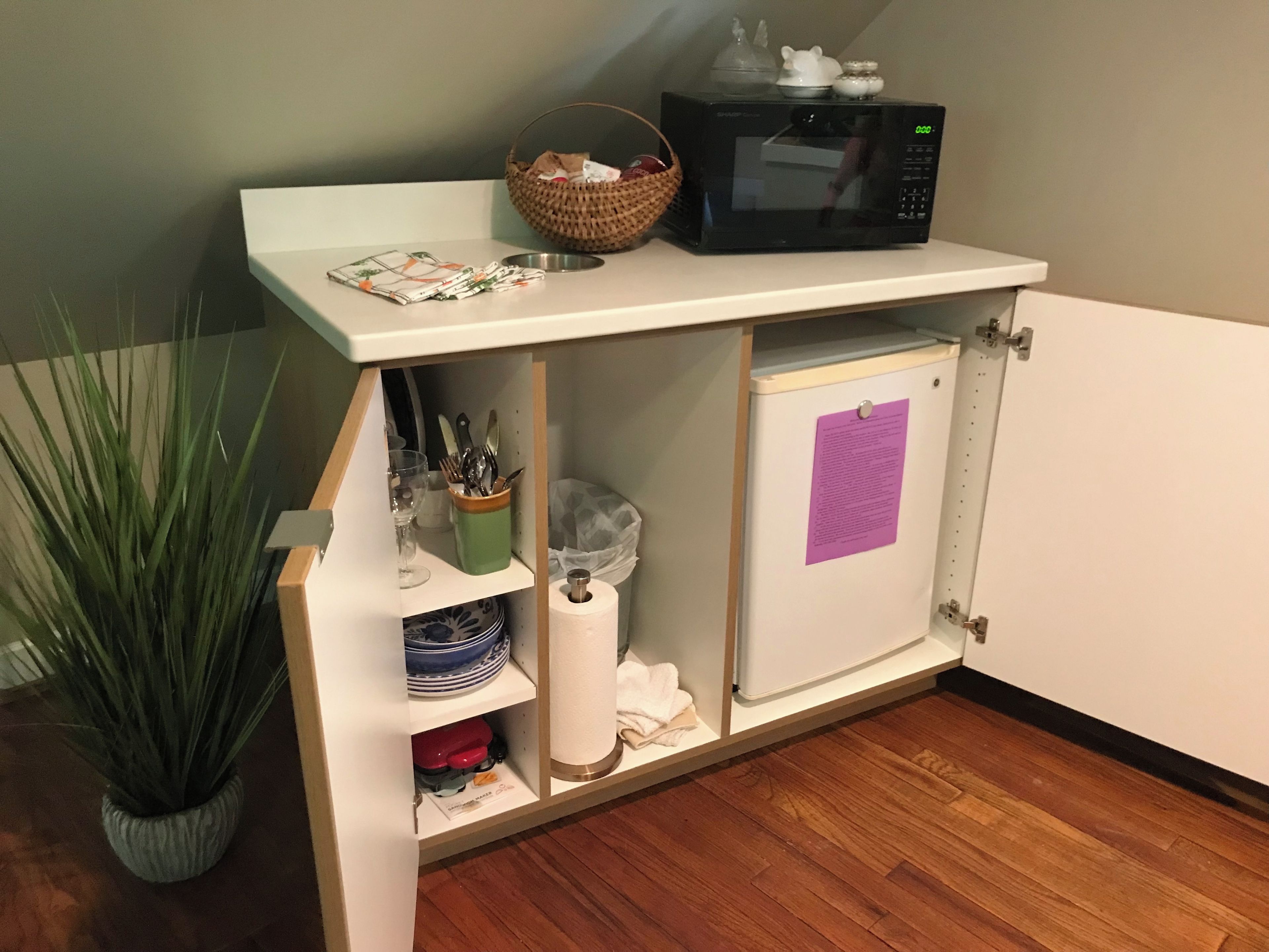 A kitchen with a microwave on a shelf, a basket, and a cabinet with a paper note.