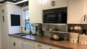 Una cocina con armarios blancos, lavavajillas, microondas y fregadero.
