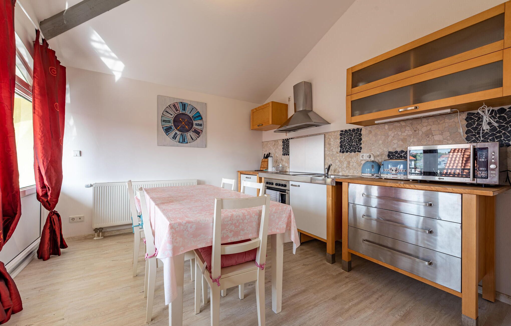 A compact kitchen with a dining table, chairs, a clock, a stove, a microwave, and a cabinet.