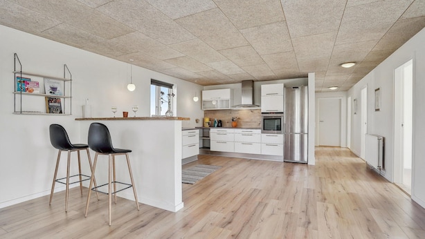 A modern kitchen with a central island, wooden flooring, and a ceiling with a geometric pattern.