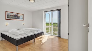A bedroom with a bed, a painting, and a view through a glass door.