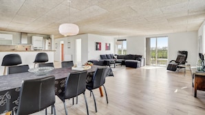 A spacious living area with a dining table, black chairs, a sofa, and a large window offering a view of the outdoors.