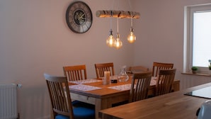 A dining area with a wooden table, six chairs, a wall clock, and a hanging light fixture. - Vacation home with its own wellness oasis for up to 7 people (Kalübbe)