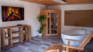 A modern bathroom with a freestanding bathtub, a wooden cabinet, a potted plant, and a large painting of a fire. - Vacation home with its own wellness oasis for up to 7 people (Kalübbe)