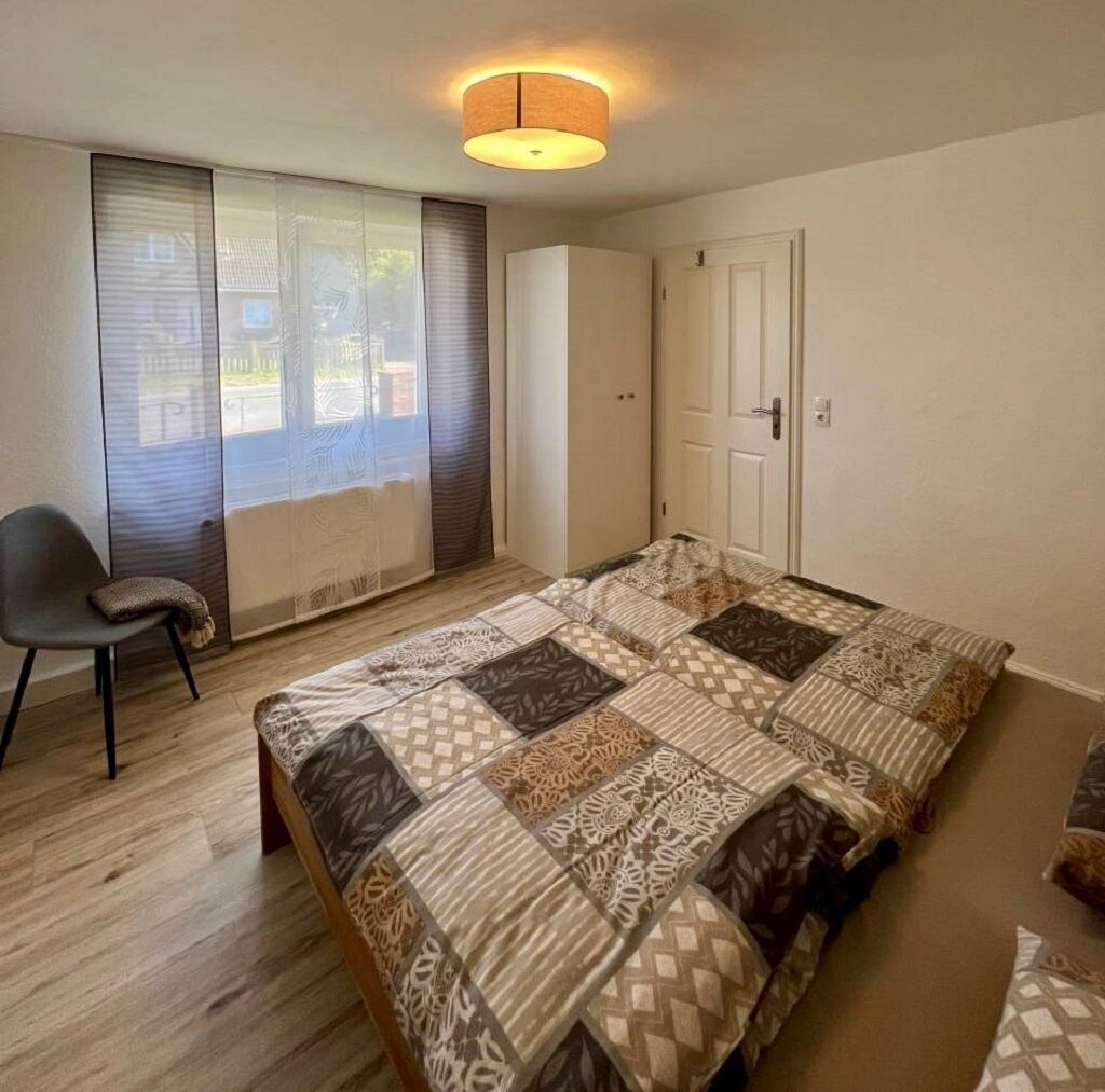 Een slaapkamer met een groot bed, een stoel, een kledingkast en een deur.