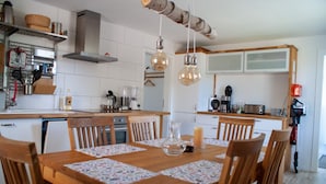 A kitchen with wooden cabinets, a central island, hanging light fixtures, and a dining table set for six. - Vacation home with its own wellness oasis for up to 7 people (Kalübbe)