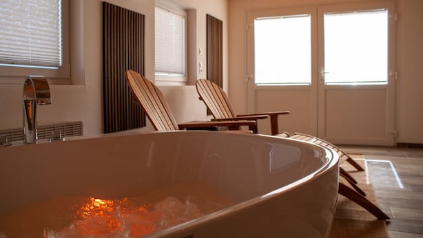 A modern bathroom with a freestanding bathtub, two wooden chairs, and a large window. - Vacation home with its own wellness oasis for up to 7 people (Kalübbe)