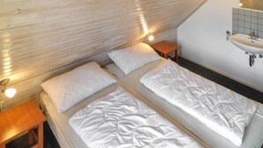 Une chambre avec deux lits, un plafond en bois, une petite table, une table de chevet et une salle de bain avec un lavabo et un miroir.