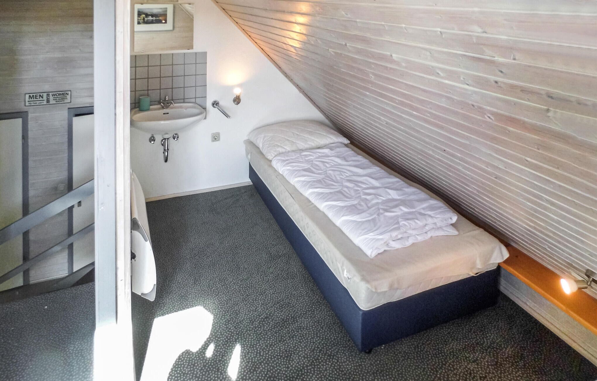 Una habitación pequeña y estrecha con una cama individual, un lavamanos y un espejo.