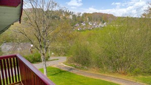 Une vue depuis un balcon donnant sur une route de campagne, avec des maisons visibles au loin et une zone herbeuse au premier plan.