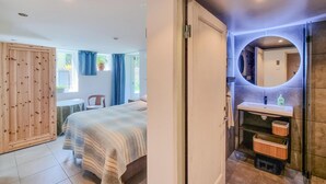 Ein Schlafzimmer mit Bett, Stuhl, einem Fenster mit Vorhängen sowie einem Badezimmer mit Waschbecken und Spiegel.