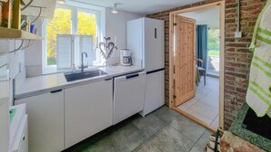 Eine moderne Küche mit weißen Schränken, einem integrierten Geschirrspüler, einer Kaffeemaschine und einem großen Fenster mit Blick auf Bäume.