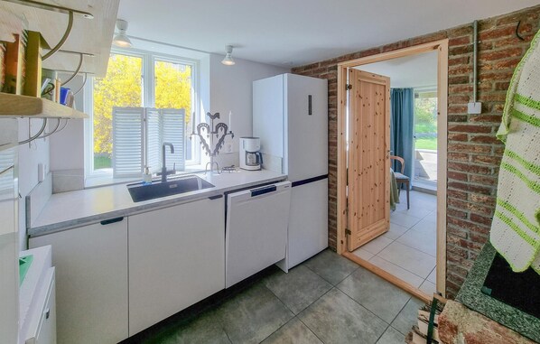 Een moderne keuken met witte kasten, een inbouwvaatwasser, een koffiezetapparaat en een groot raam met uitzicht op bomen.