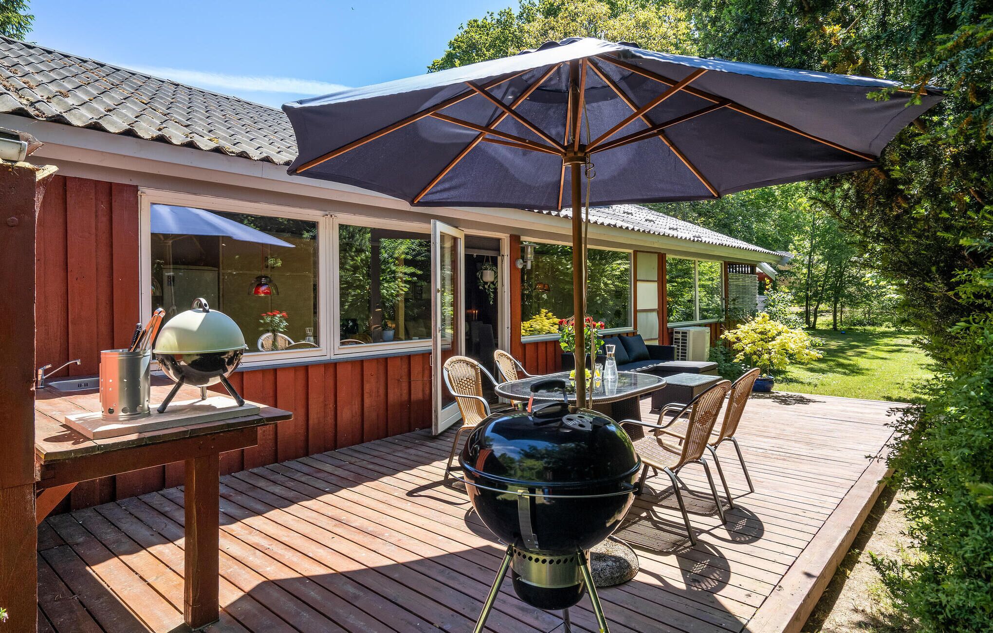 A wooden deck with a grill and outdoor furniture, a covered patio area, and a view of the surrounding greenery.