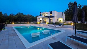 Ein modernes, zweistöckiges Haus mit Pool, Sitzgelegenheiten im Freien und guter Beleuchtung.