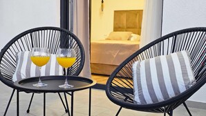Zwei Korbstühle mit gestreifter Polsterung, ein kleiner Tisch und zwei Gläser Orangensaft auf einem Balkon.