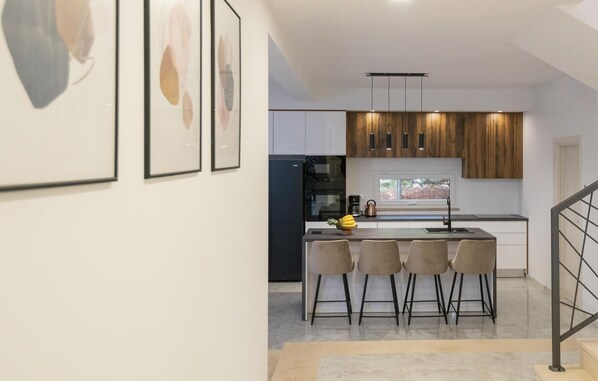A modern kitchen with a central island, bar stools, and a dining area.