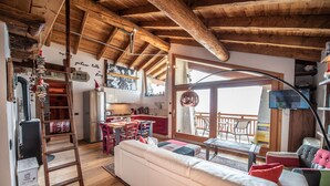 Un salon chaleureux avec un plafond en bois, un canapé blanc et un coin repas comprenant une table et des chaises.