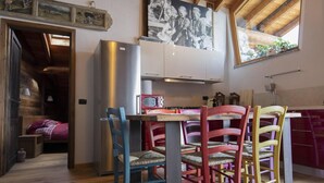Une cuisine chaleureuse avec des poutres en bois, une table à manger entourée de chaises colorées, un réfrigérateur et une grande fenêtre.