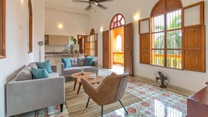 A spacious living room with a sofa, armchair, and coffee table, a ceiling fan, and large windows with wooden shutters. - 2CM-J1 APARTAMENTO EN GETSEMANI CON WIFI (Cartagena)