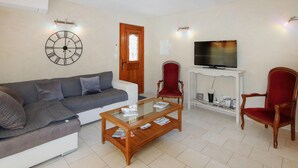 A living room with a grey sofa, a wooden coffee table, two red armchairs, a TV on a white stand, and a wall clock. - 2 bedroom cozy home in Rousset les Vignes (Rousset les Vignes)